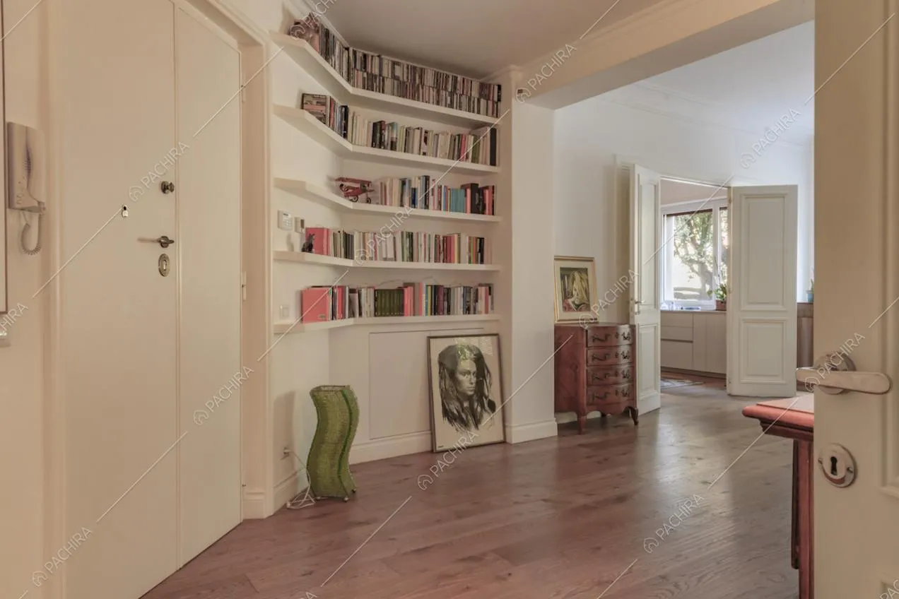 Atrio dalle pareti bianche con boiserie, con libreria e vista sulla cucina