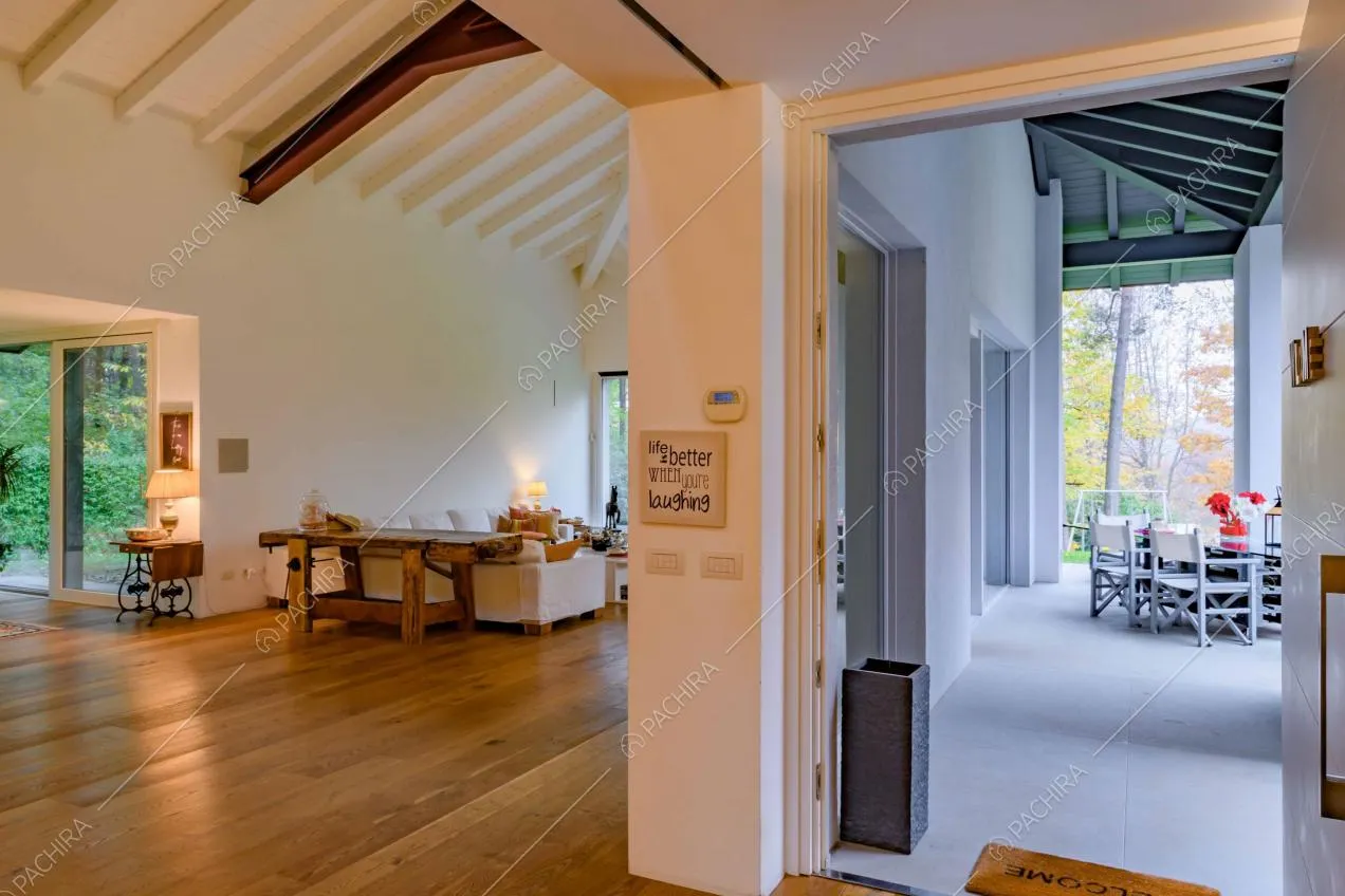Vista sul salotto con pavimento in parquet e sulla veranda total white con soffitto in travi in legno a vista