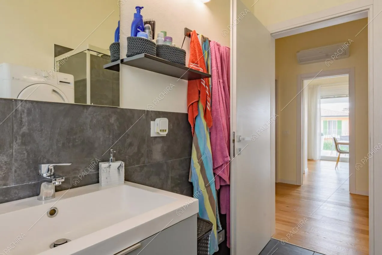 Bagno con piastrelle grigie e vista sul corridoio con pavimento in parquet