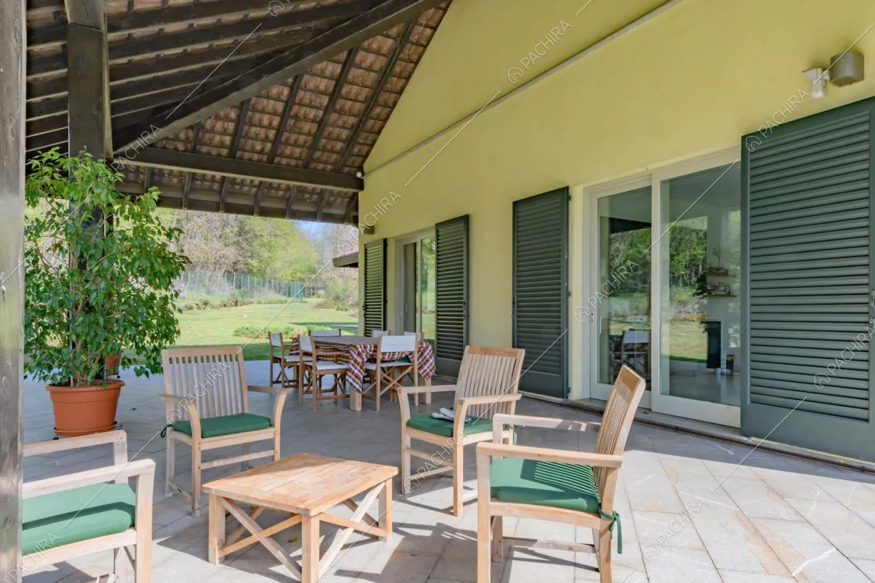 Sedie e tavolino nella veranda con soffitto in travi in legno a vista ed esterni gialli