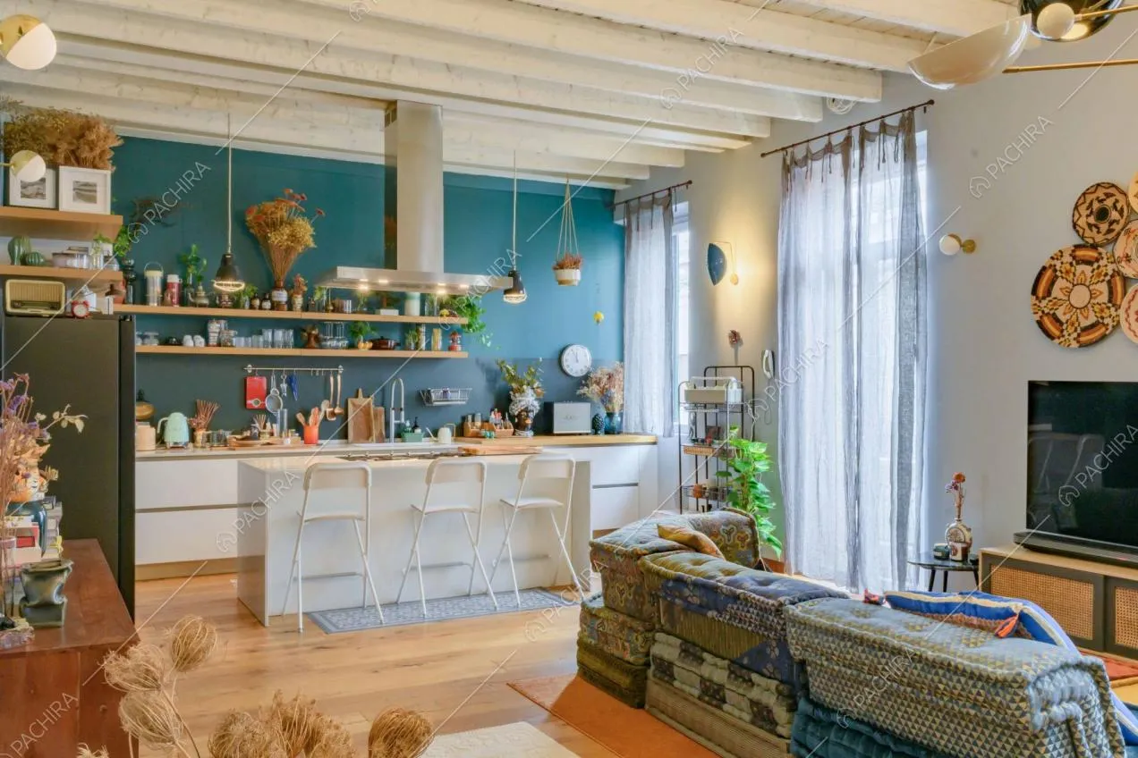 Luminosa sala con cucina a vista, parete blu e soffitto bianco in travi in legno a vista