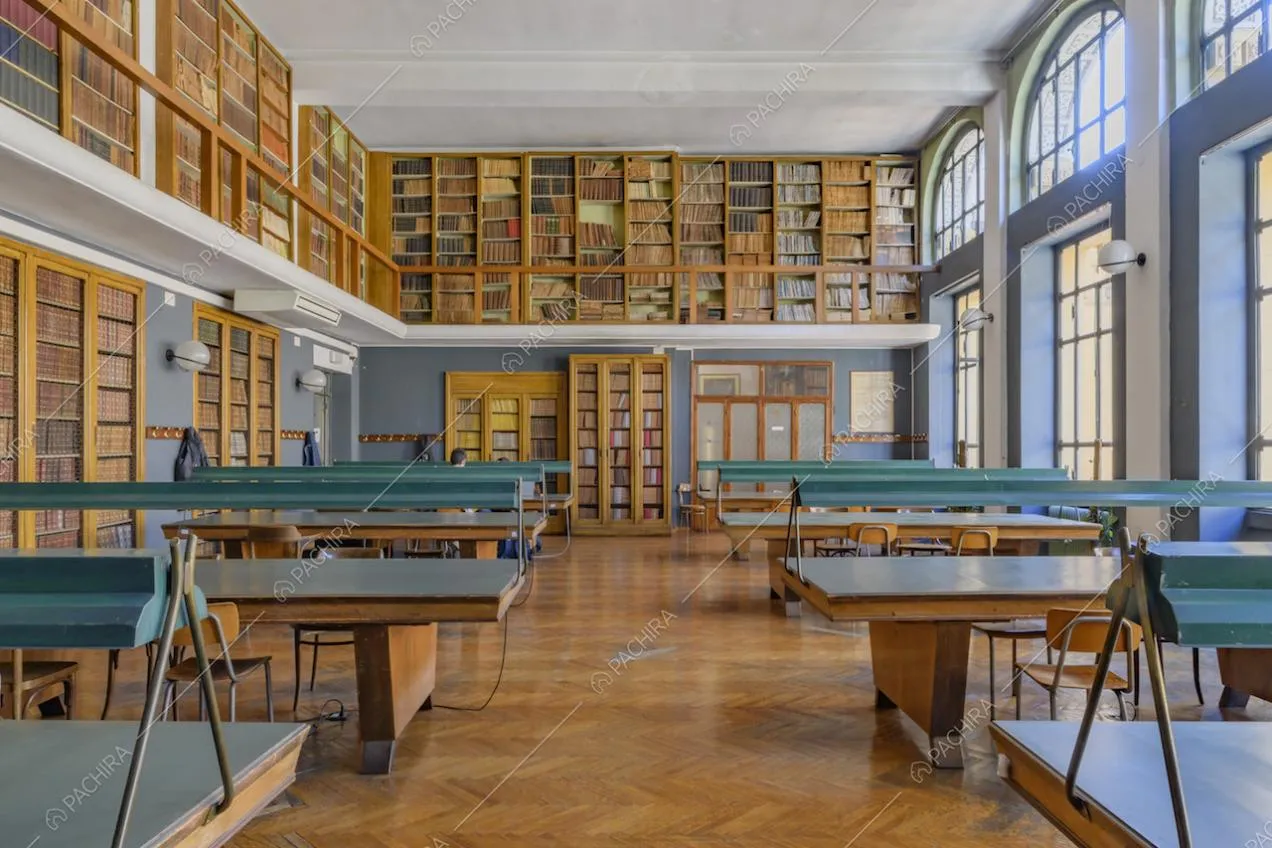 Biblioteca illuminata da vetrate con pavimento in parquet a spina di pesce e librerie sulla balconata