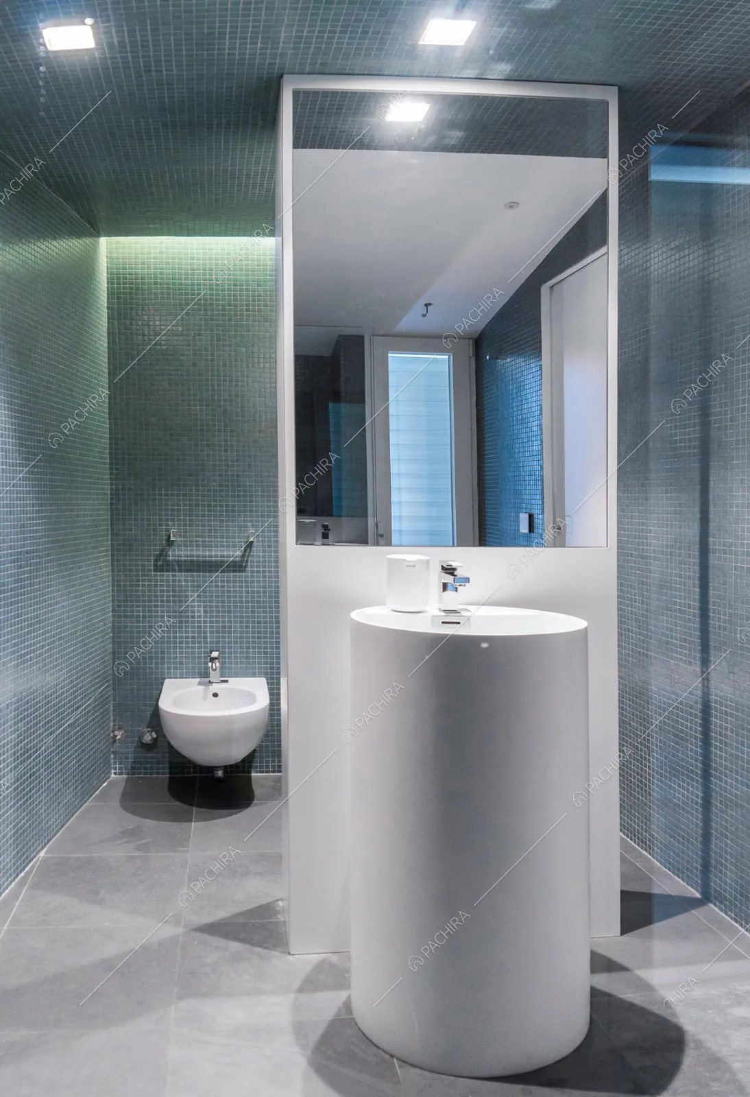 Bagno con pavimento grigio, piccole piastrelle sui toni del blu e lavabo bianco cilindrico