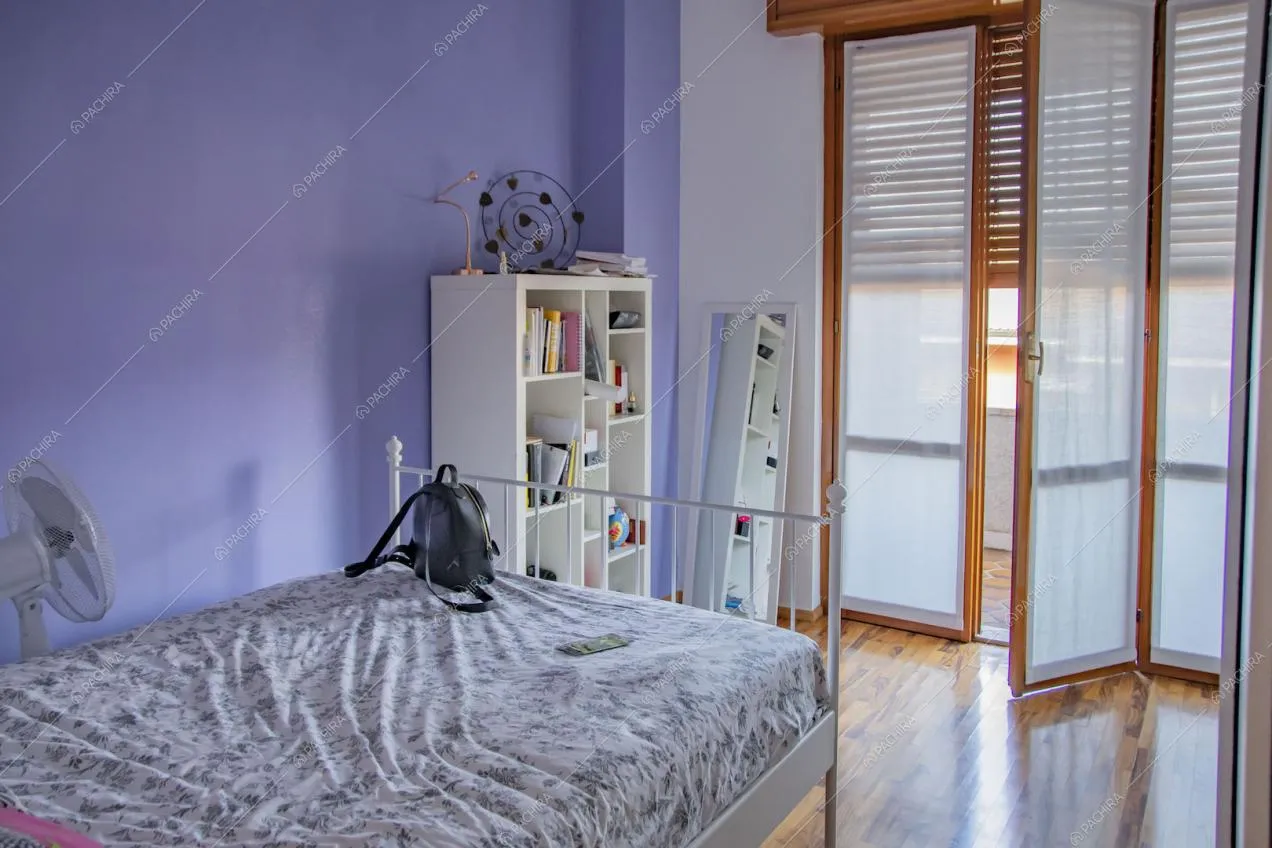 Camera da letto con parete lilla, pavimento in parquet e porta-finestra