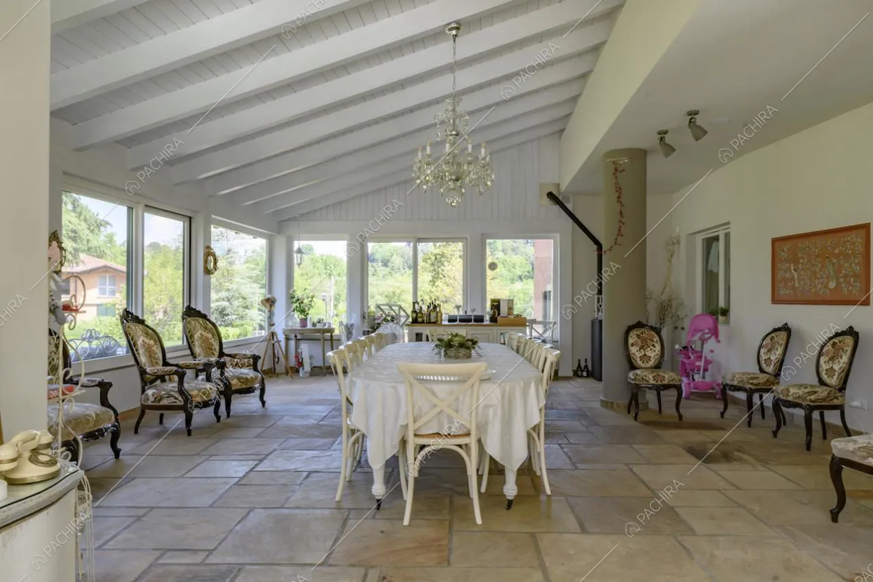 Ampia veranda con travi in legno bianco a vista, pavimento in pietra e grande tavolo da pranzo