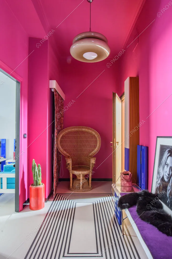 Corridoio dalle pareti fucsia con poltrona di vimini di design e disegno geometrico sul pavimento