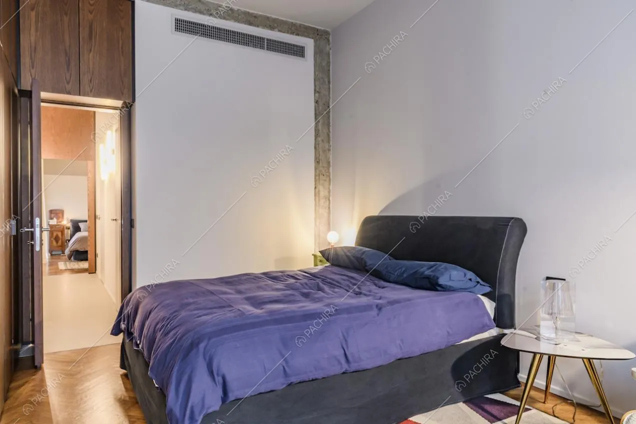 Camera da letto con lenzuola viola e pavimenti in parquet