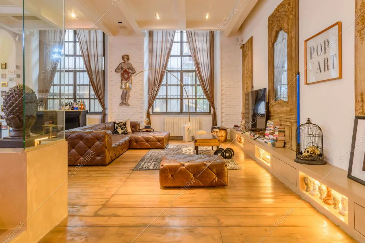 Pavimento in parquet nel salotto con divano marrone in pelle con pouf e specchio con cornice dorata