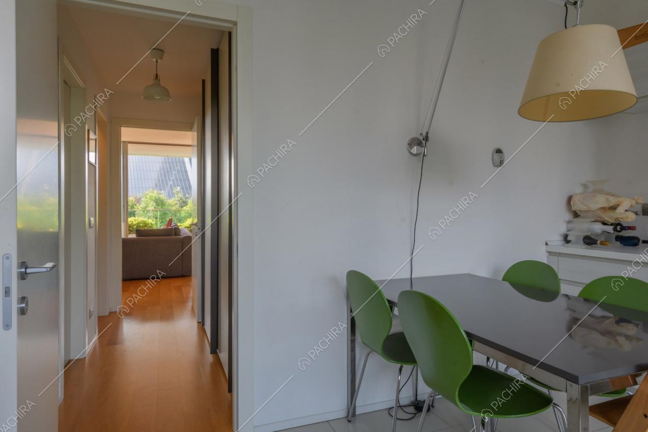 Tavolo da pranzo nero, sedie verdi e scorcio sulla zona living con pavimento in parquet