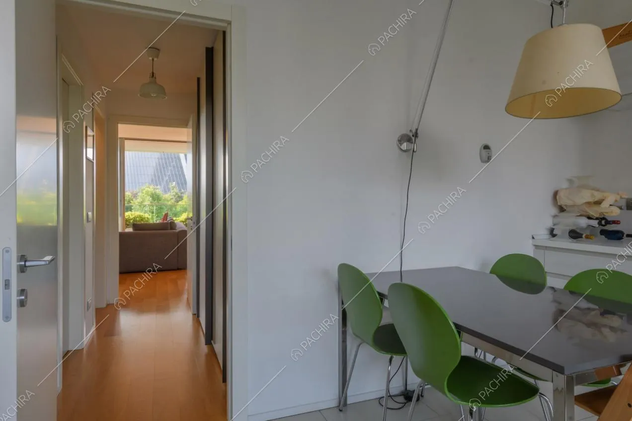 Tavolo da pranzo nero, sedie verdi e scorcio sulla zona living con pavimento in parquet