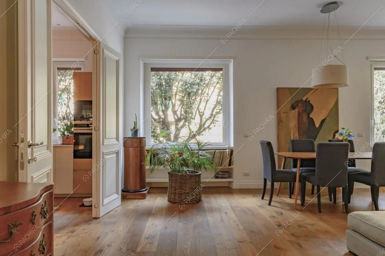 Sala dalle pareti bianche con pavimento in parquet, tavolo da pranzo in legno e vista sulla cucina