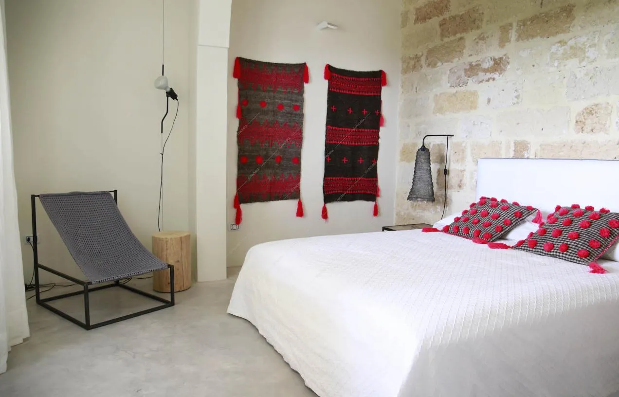 Letto matrimoniale nella camera con pavimento in cemento lisciato e parete con mattoni a vista