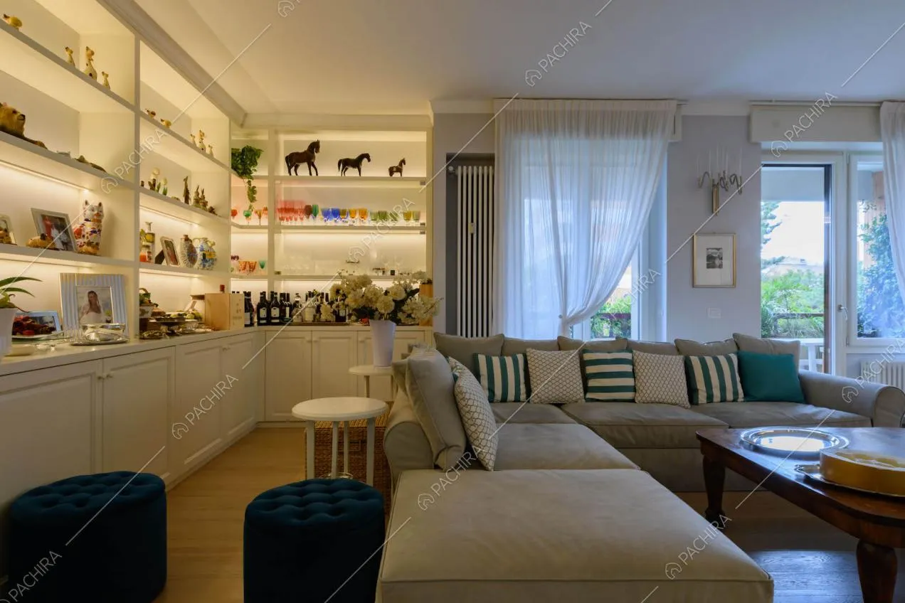 Divano grigio angolare nel luminoso salotto con libreria e pavimento in parquet