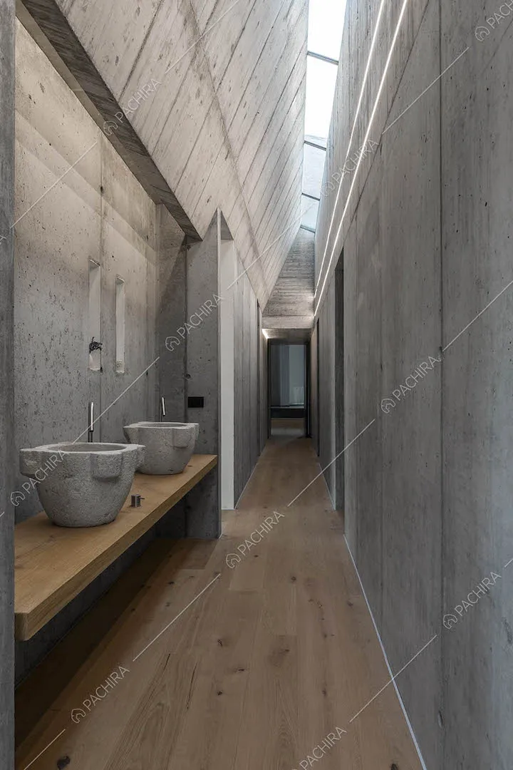 Lungo bagno con pareti in cemento e pavimento in parquet illuminato dai lucernari