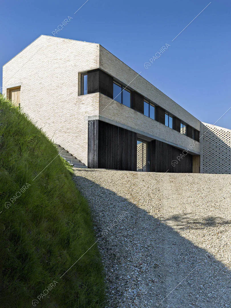 Dal vialetto in ciottolato vista sulla villa con pareti in mattoni e vetrate