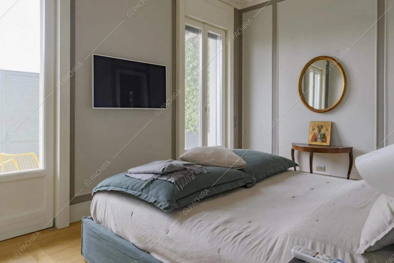 Camera da letto matrimoniale con boiserie alle pareti, pavimento in parquet e porte-finestre che portano alla terrazza