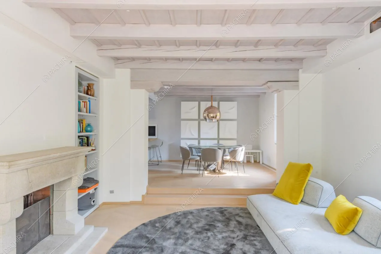 Camino nel luminoso salotto con pavimento in parquet, divano e tavolo da pranzo