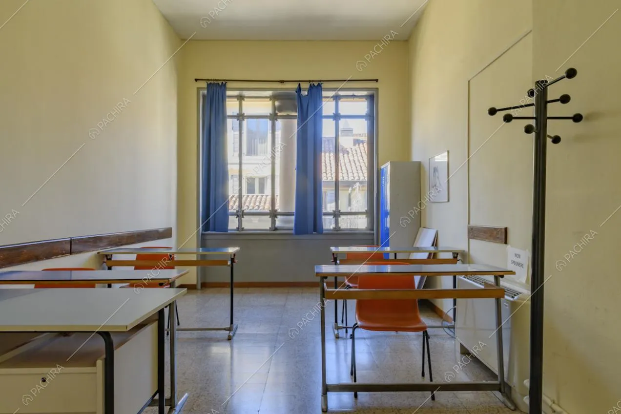 Piccola aula dalle pareti gialle con banchi d'epoca, pavimento in piastrelle e finestra