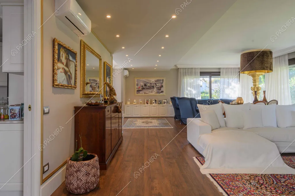 Zona living con divano angolare bianco, pavimento in parquet e scorcio sulla cucina