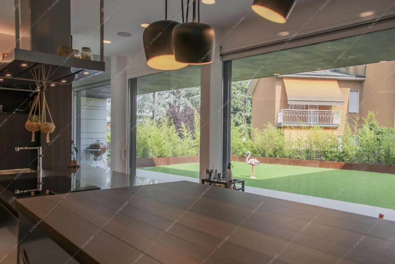 Dall'isola in legno della cucina vista sul giardino tramite le grandi vetrate