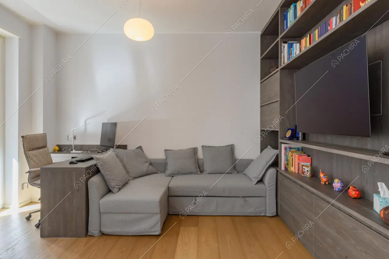 Divano grigio angolare, scrivania e libreria nella luminosa sala con pavimento in parquet