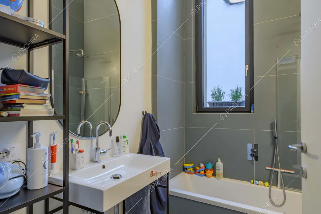 Pareti bianche e in grandi piastrelle grigie nel bagno con vasca