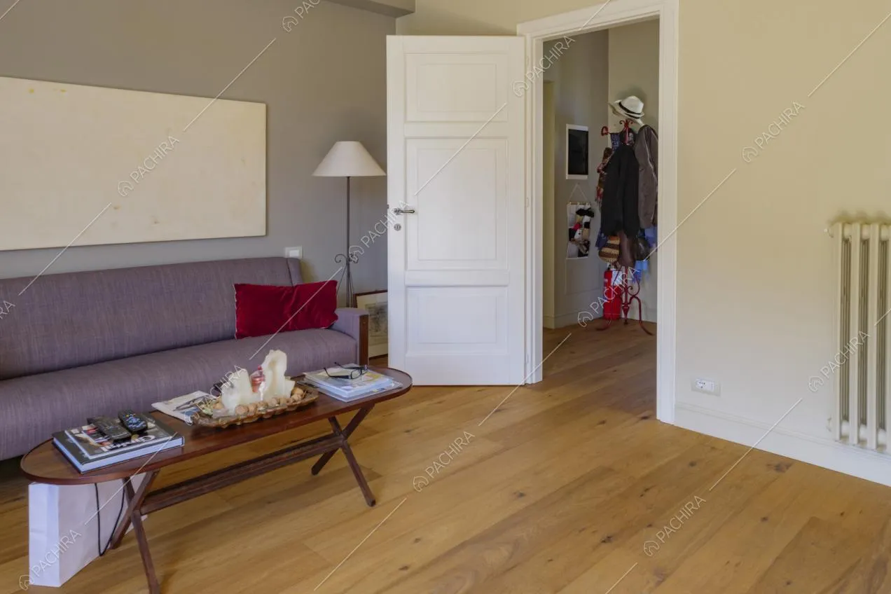 Dal salotto con divano viola e pavimento in parquet vista sull’ingresso
