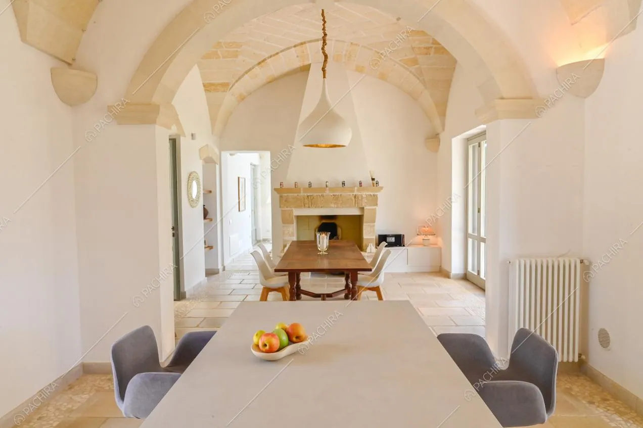 Nell'ampio salone con soffitto ad arco, due tavoli da pranzo, camino e pareti bianche