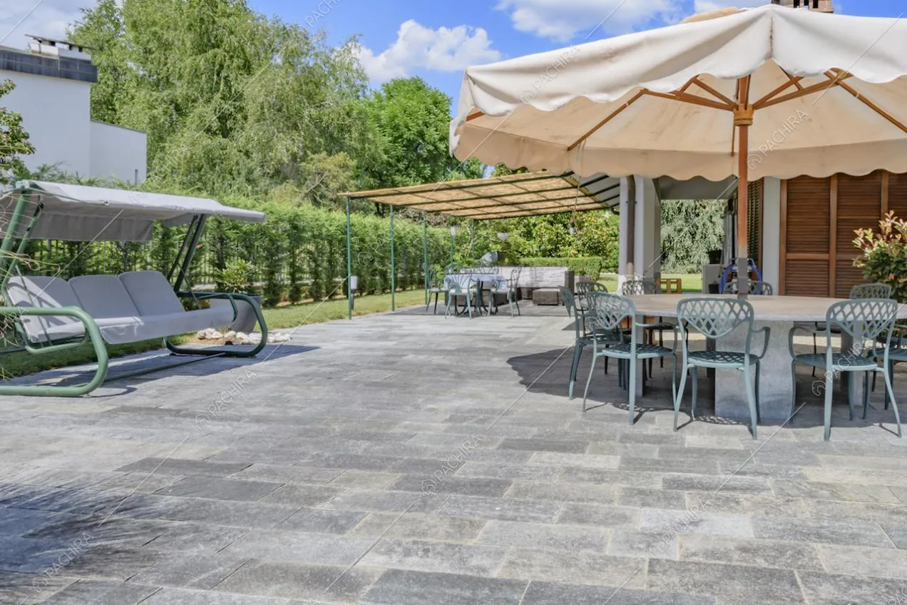 Giardino con pavimento in pietra, dondolo, ombrellone e vista sulla veranda aperta