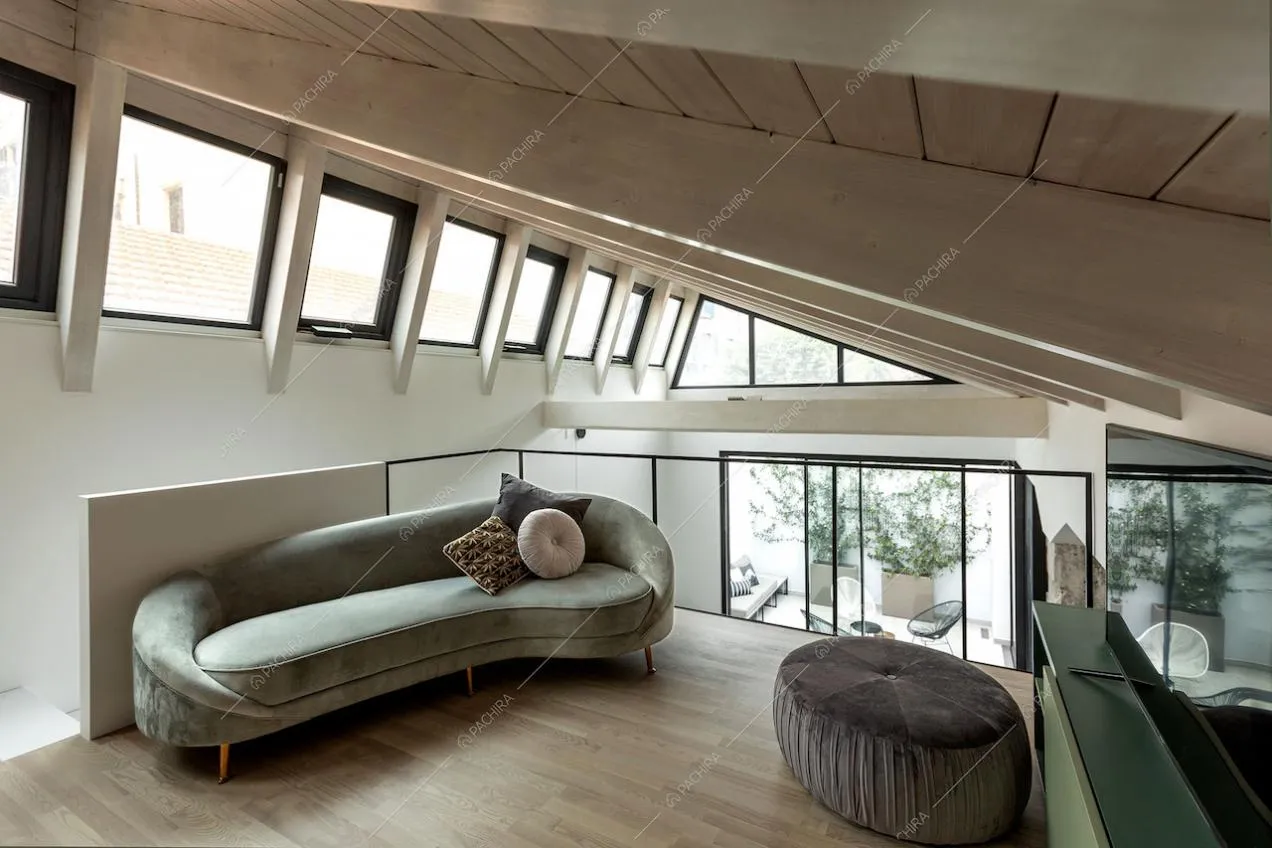 Divano di velluto verde sul soppalco con pavimento in parquet e soffitto con travi a vista in legno