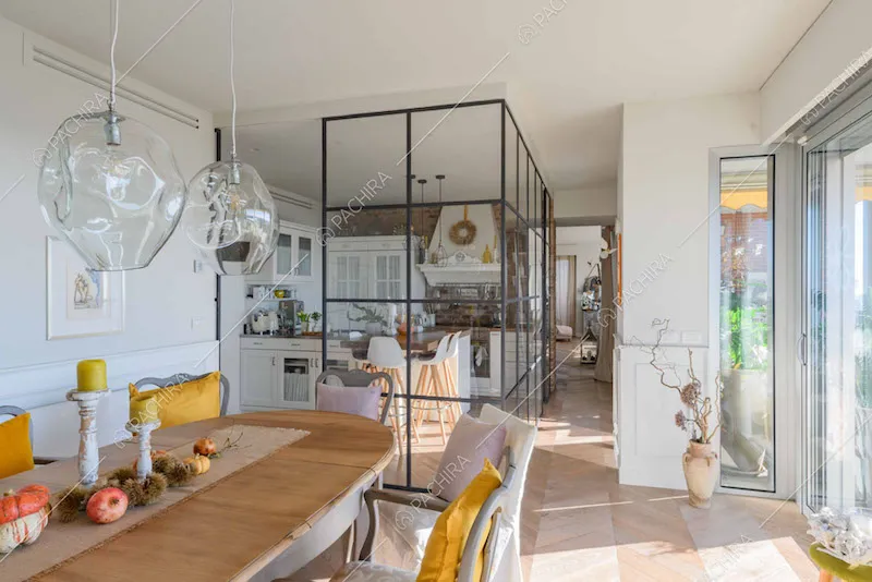 Tavolo da pranzo in legno nella sala con cucina a vista separata da una parete vetrata