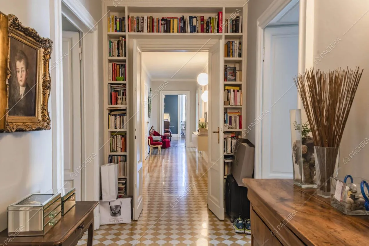 Libreria bianca incornicia la porta del lungo corridoio con pavimento a scacchi