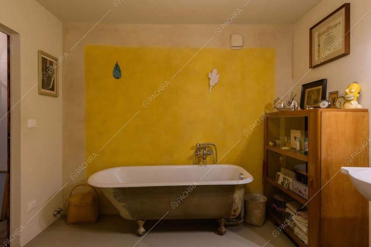 Parete gialla délabré del bagno con vasca e pavimento grigio in resina