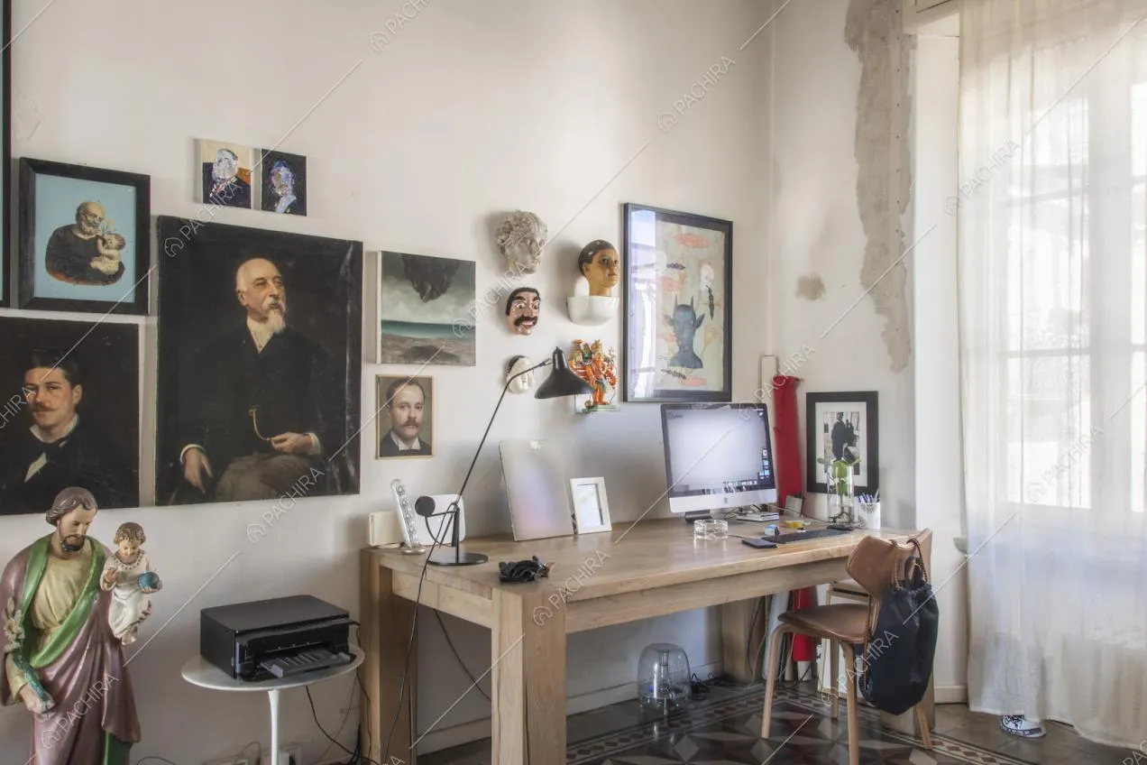 Scrivania in legno chiaro con computer e ritratti d'epoca appesi alla parete