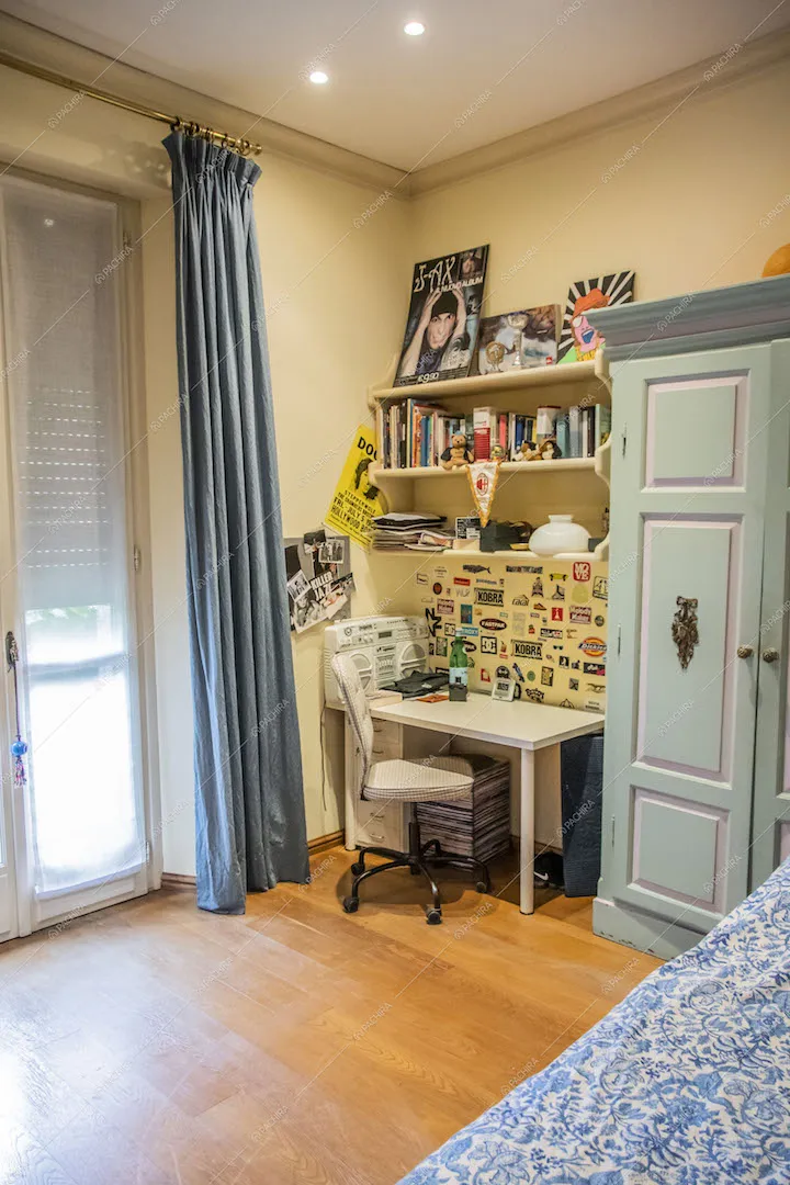 Camera da letto con scrivania bianca, pavimento in parquet e porta-finestra