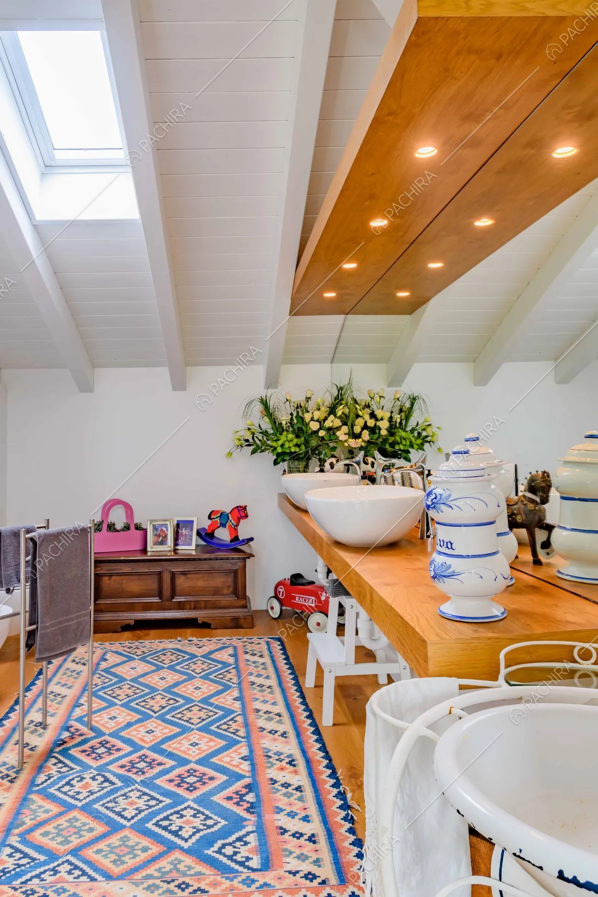 Bagno con grande specchio, soffitto bianco con travi in legno a vista e lucernario che illumina lo spazio
