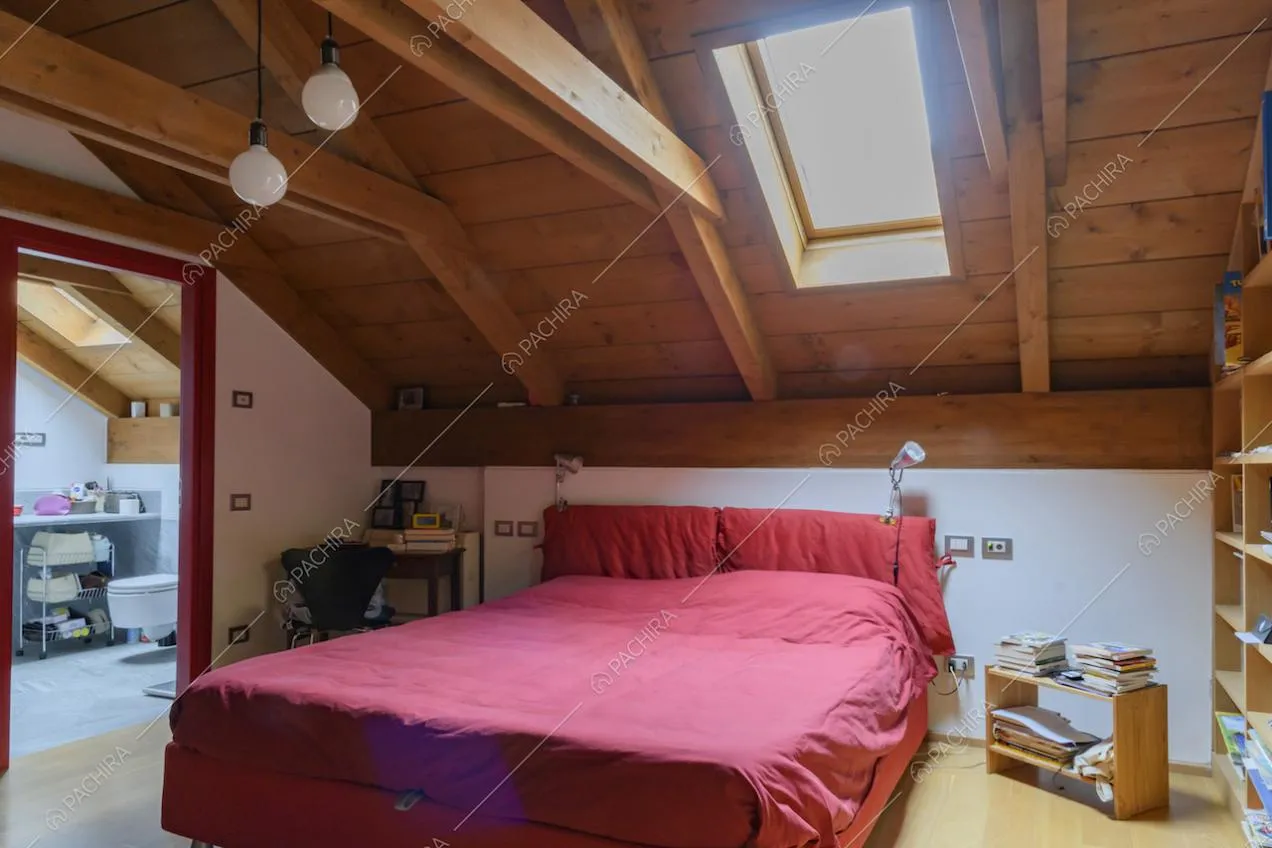 Camera da letto con bagno privato illuminata dal lucernario sul soffitto in travi in legno a vista