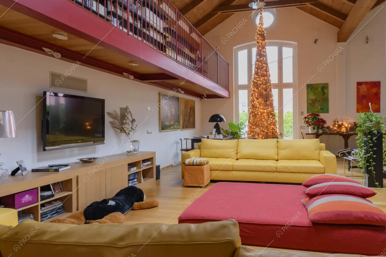 Divani gialli e pouf rosso nel salone con pavimento in parquet, vetrate e soppalco dagli infissi rossi