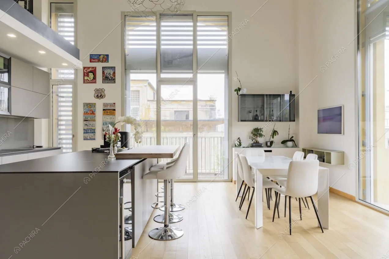 Isola e tavolo da pranzo bianco nella cucina illuminata dalle porte-finestre con vista sul giardino