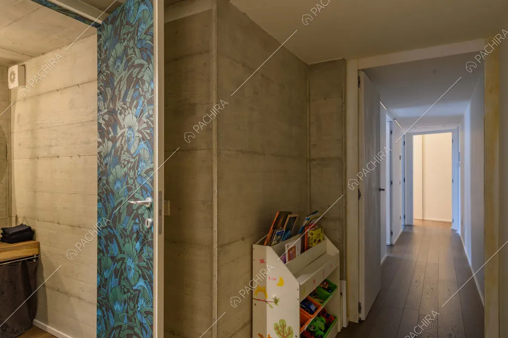 Pareti in cemento, porta con carta da parati e vista sul lungo corridoio