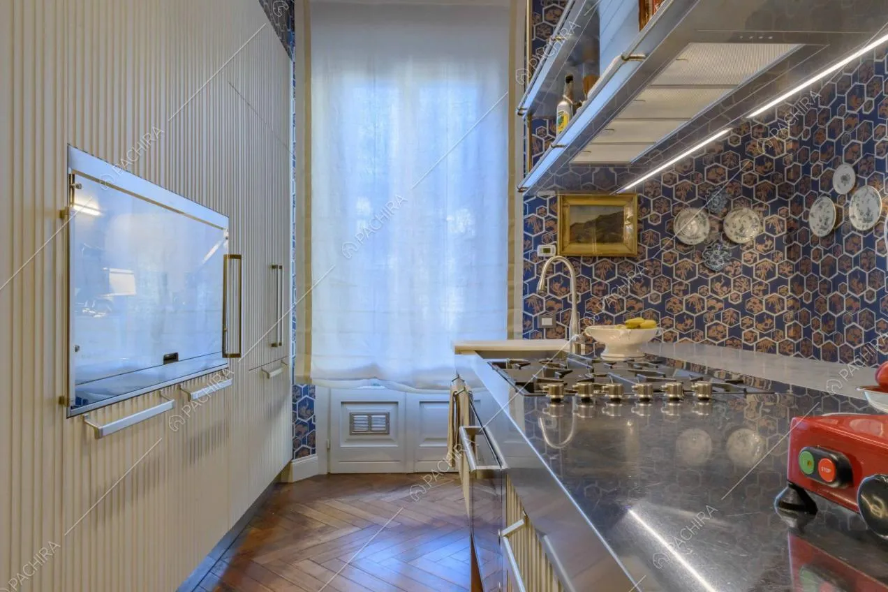 Isola in metallo, con fornelli a gas e lavandino nella cucina con pavimento in parquet e porta-finestra