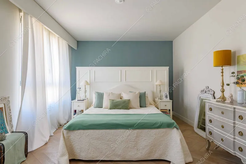 Letto matrimoniale con testata bianca con boiserie, parete blu e vetrate