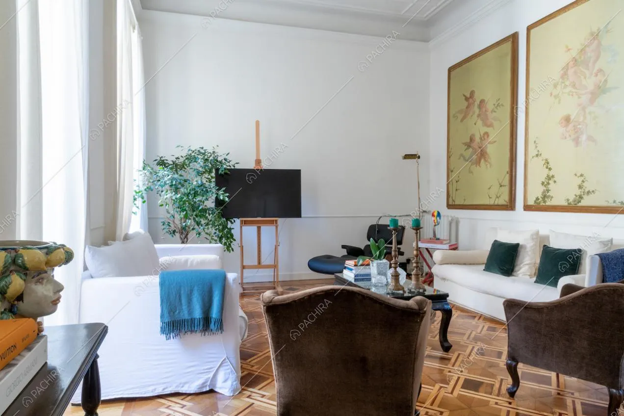 Salotto con pavimento in parquet, pareti bianche con boiserie e ampie vetrate che lo illuminano