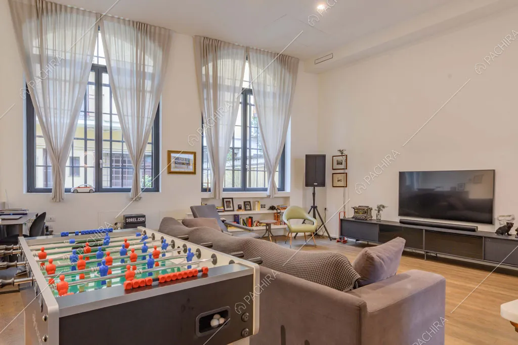 Divano grigio nella zona living con finestre industriali e pavimento in parquet