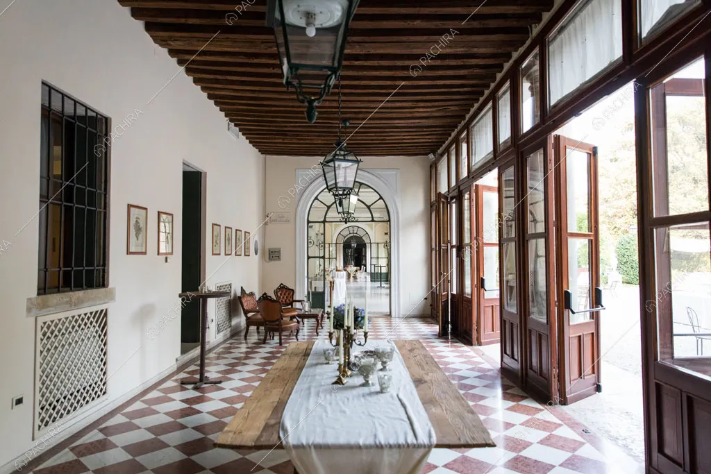 Pavimento a scacchi marrone e bianco nel corridoio con travi a vista sul soffitto e porte-finestre