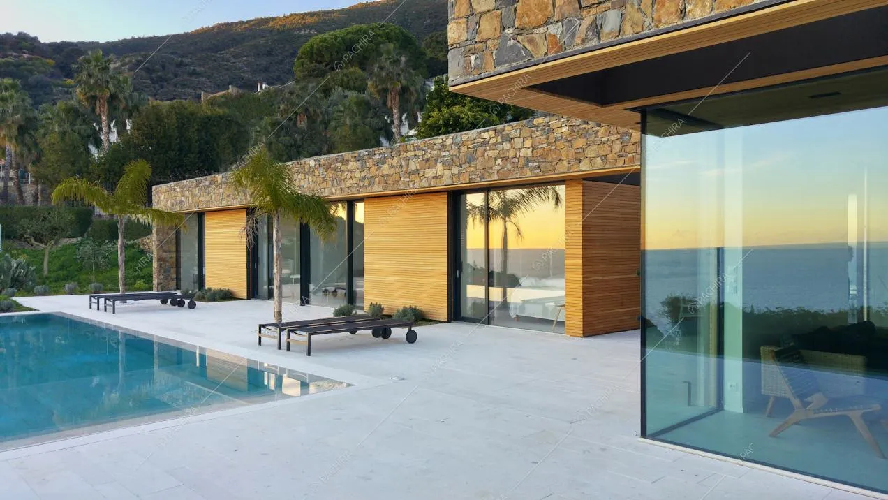 Terrazza con pavimentazione bianca, piscina a sfioro, lettini neri e palme e vetrate