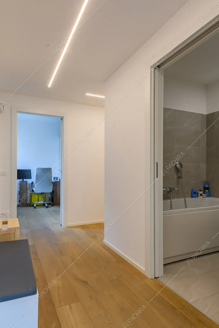 Dal corridoio con pareti bianche, pavimento in parquet e vista sul bagno