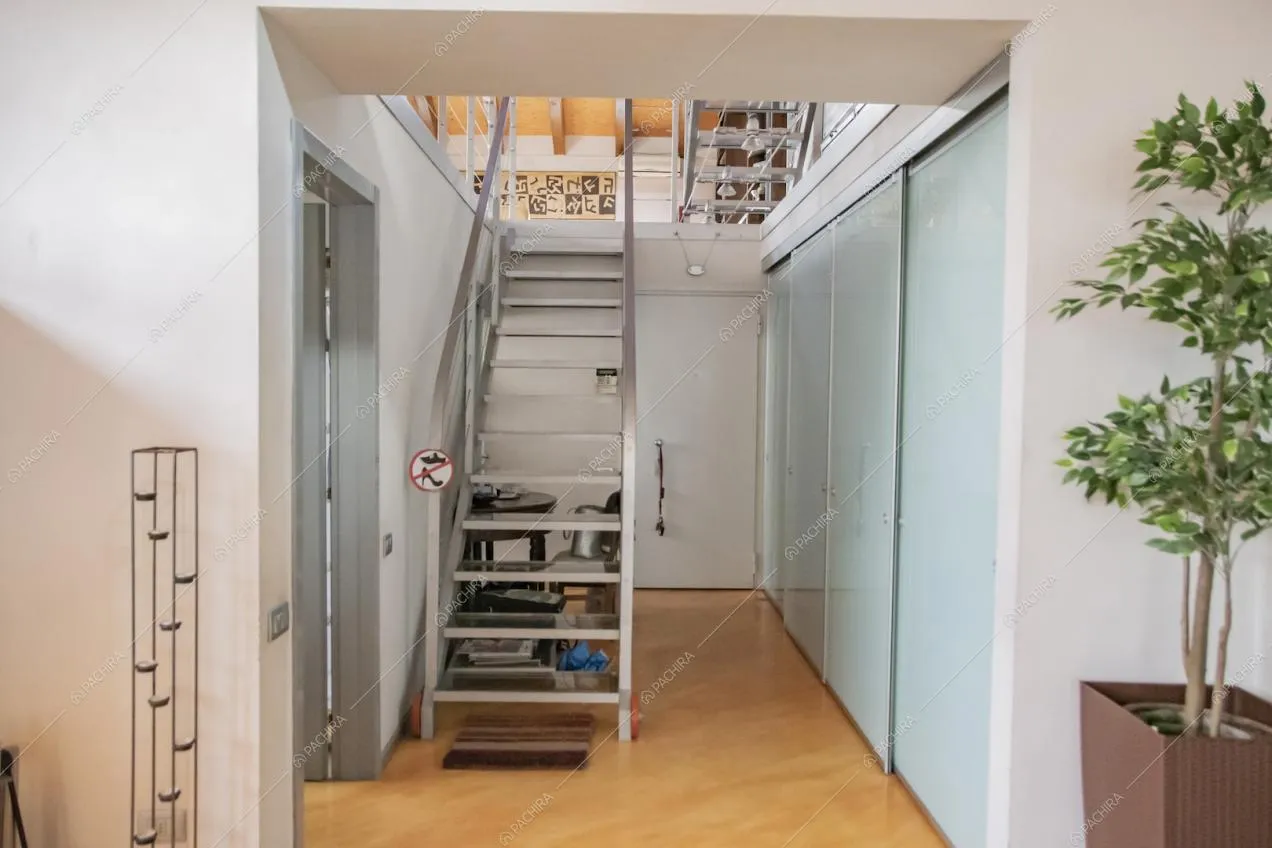 Vista sulle scale per salire sul solaio nel corridoio dalle pareti bianche e pavimento in parquet