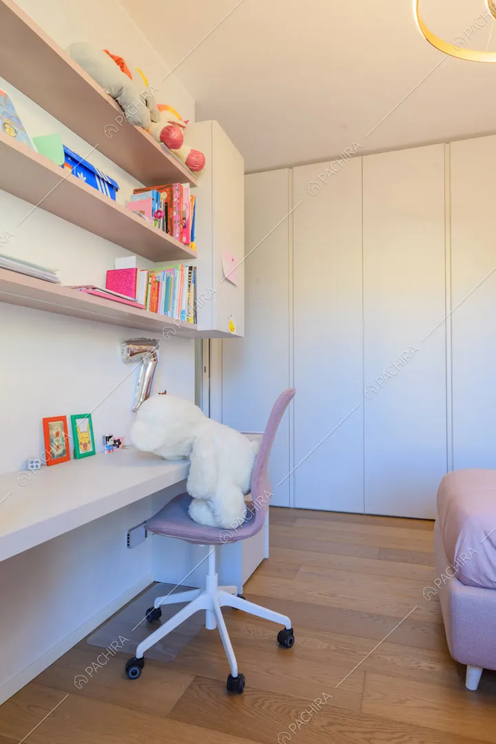 Sedia rosa e scrivania nella camera da letto con armadi a muro e pavimento in parquet