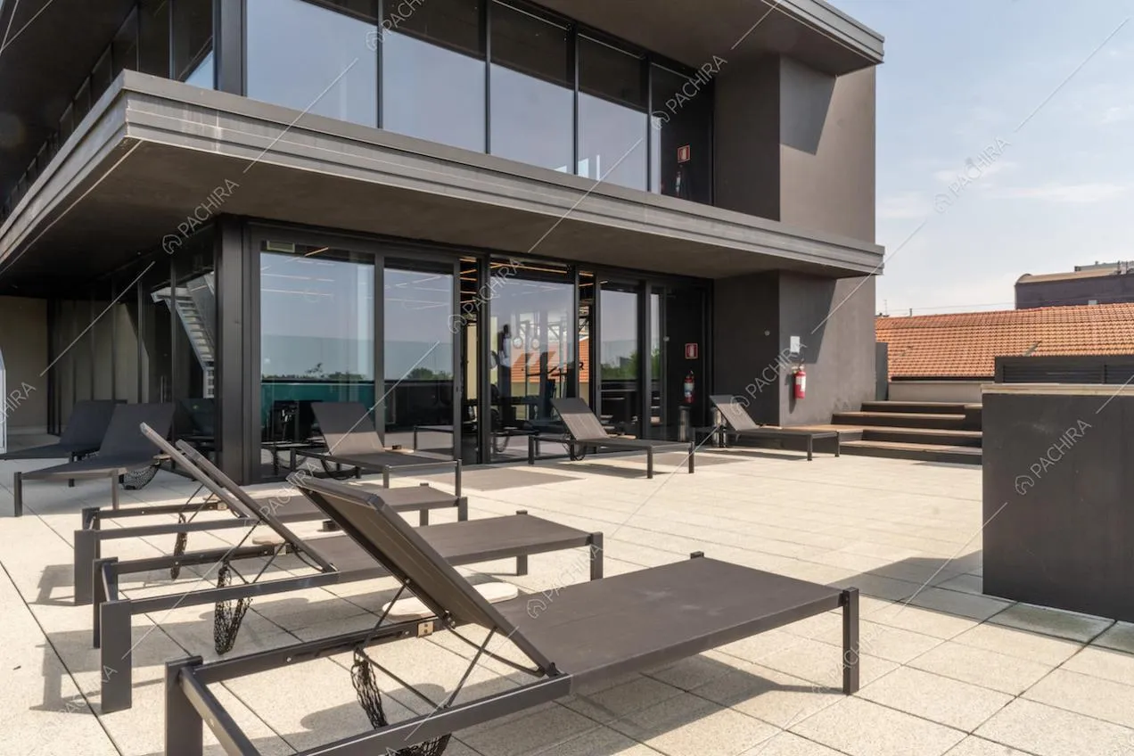 Terrazza con lettini neri, pavimento in piastrelle bianche e vista sulle vetrate dell'attico e superattico